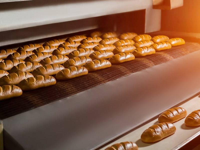 Fresh buns from the oven. Conveyor with bread. Baking bread. Workshop for production of bread. White bread in the oven. Hot buns. Confectionery.